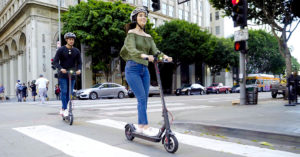 Couple crossing the street on their Swagger 5, wearing a helmet to prevent head injuries