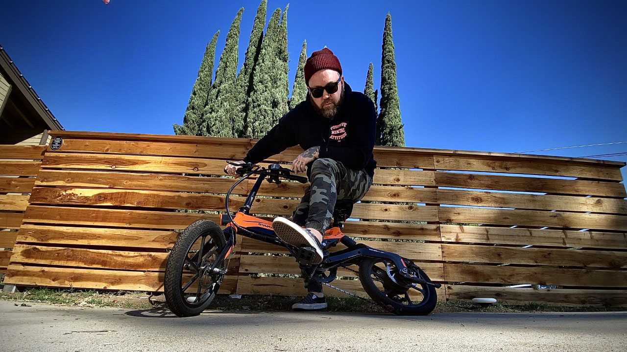 Terry Corso from Alien Ant Farm Terry Corso on Swagtron EB7 Plus electric bike in front of a fence with blue sky background.