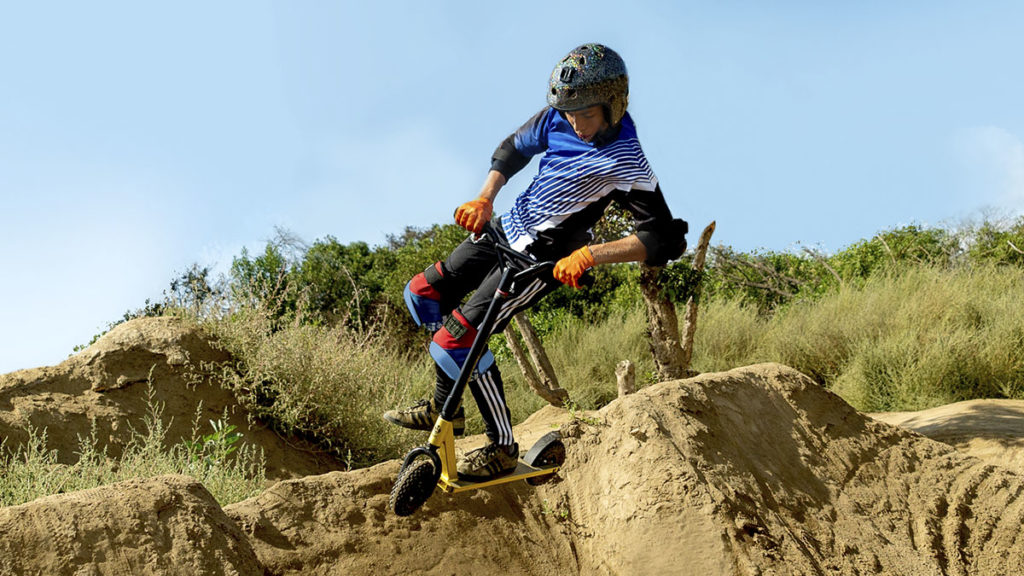Young man riding the KR-1 dirt stunt scooter on a trail.